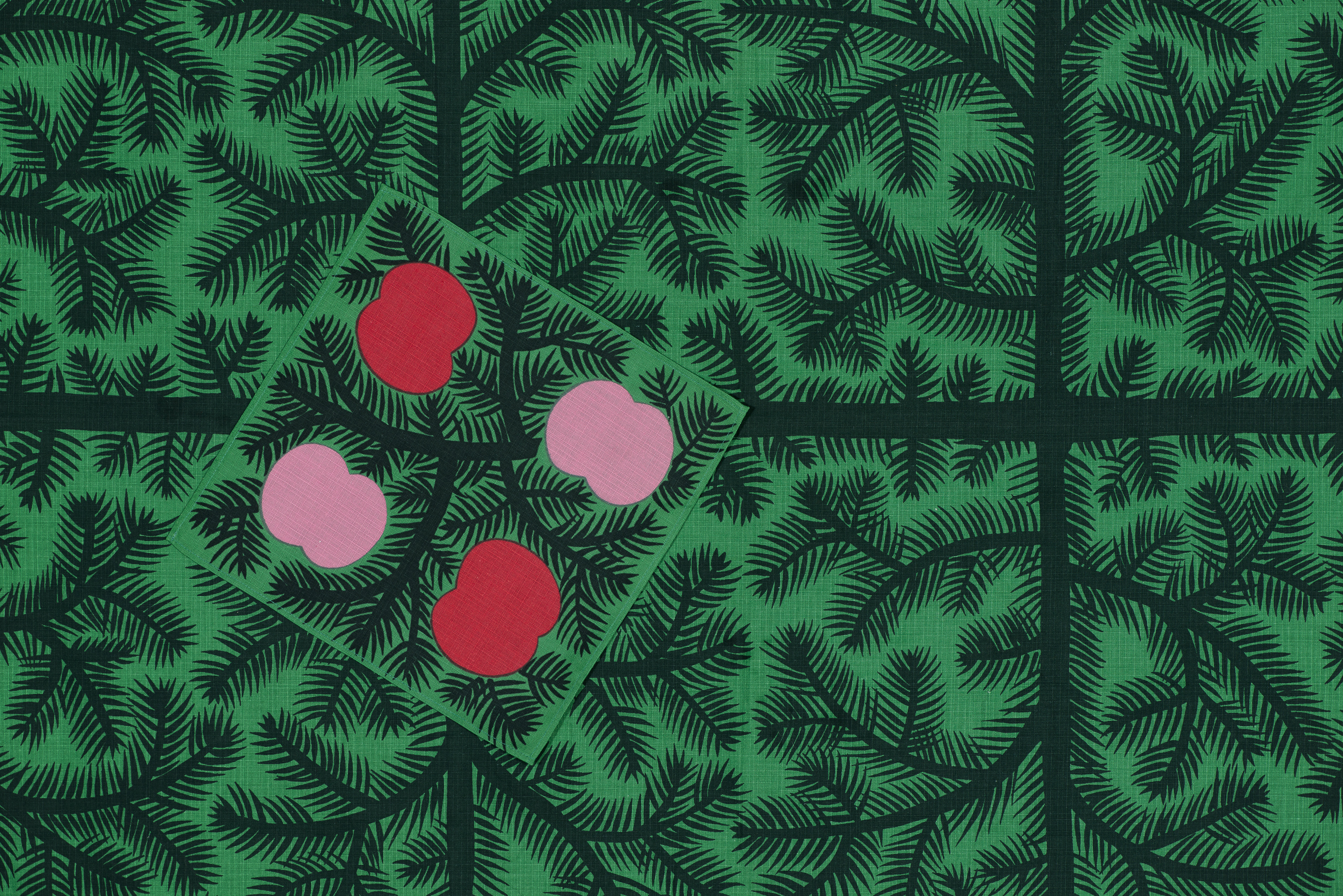 En grön julduk med grankvistmönster och en romb med fyra rosa och röda äppelliknande former på