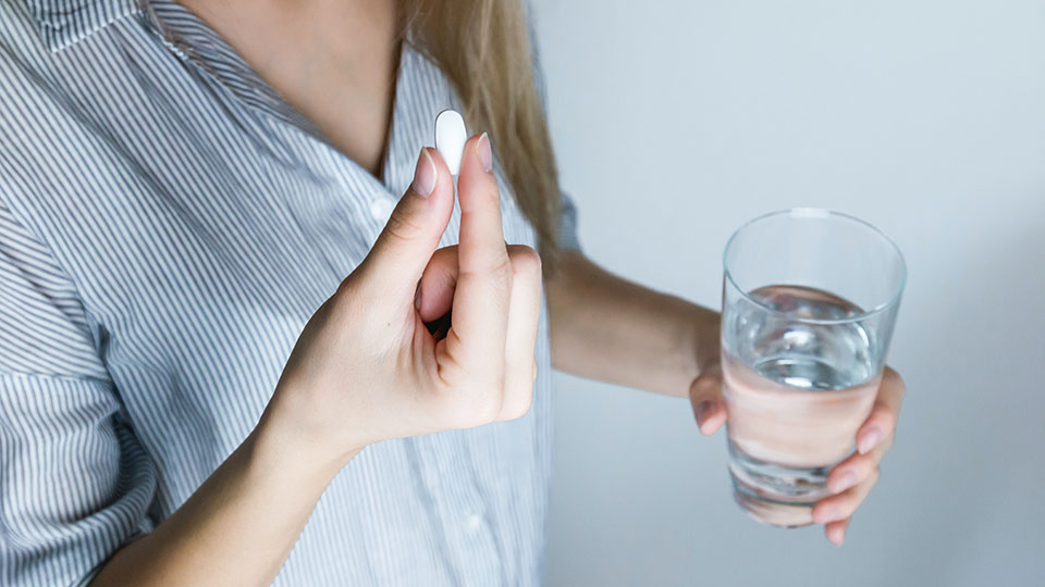 Foto på person som håller i ett glas vatten och ett piller