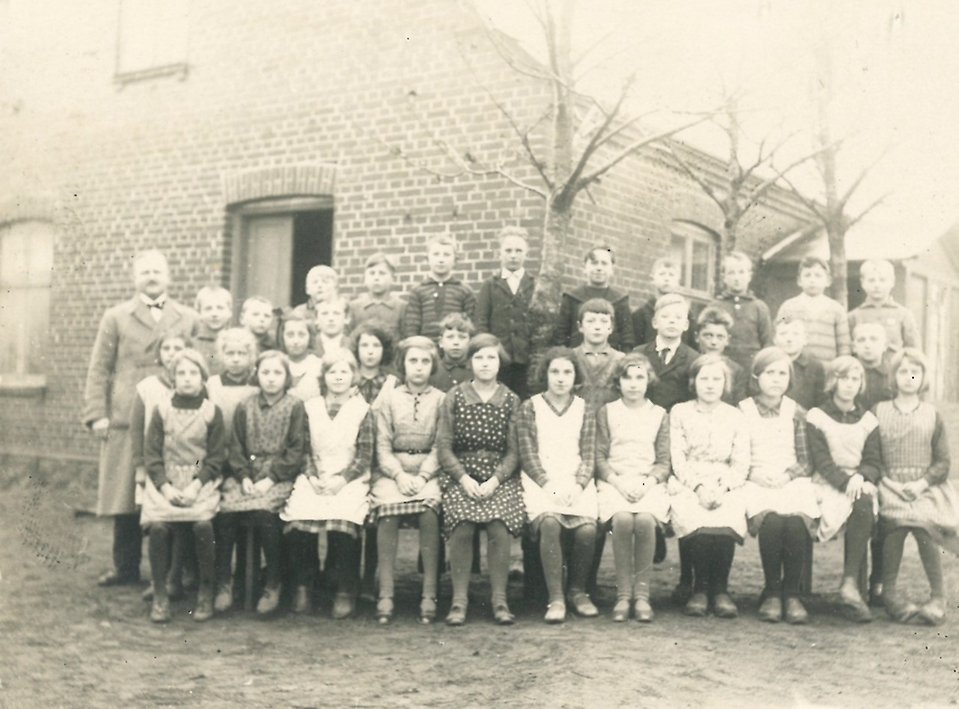 Skolklass med elever sitter tillsammans framför en byggnad.