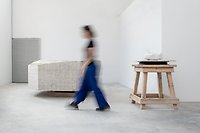 Foto med en kvinna som går i ett vitt rum med ett bord, en stor sten och en dörr