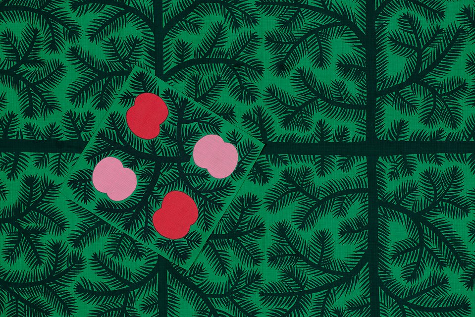 En grön julduk med grankvistmönster på, samt en romb med fyra rosa och röda äppelliknande former