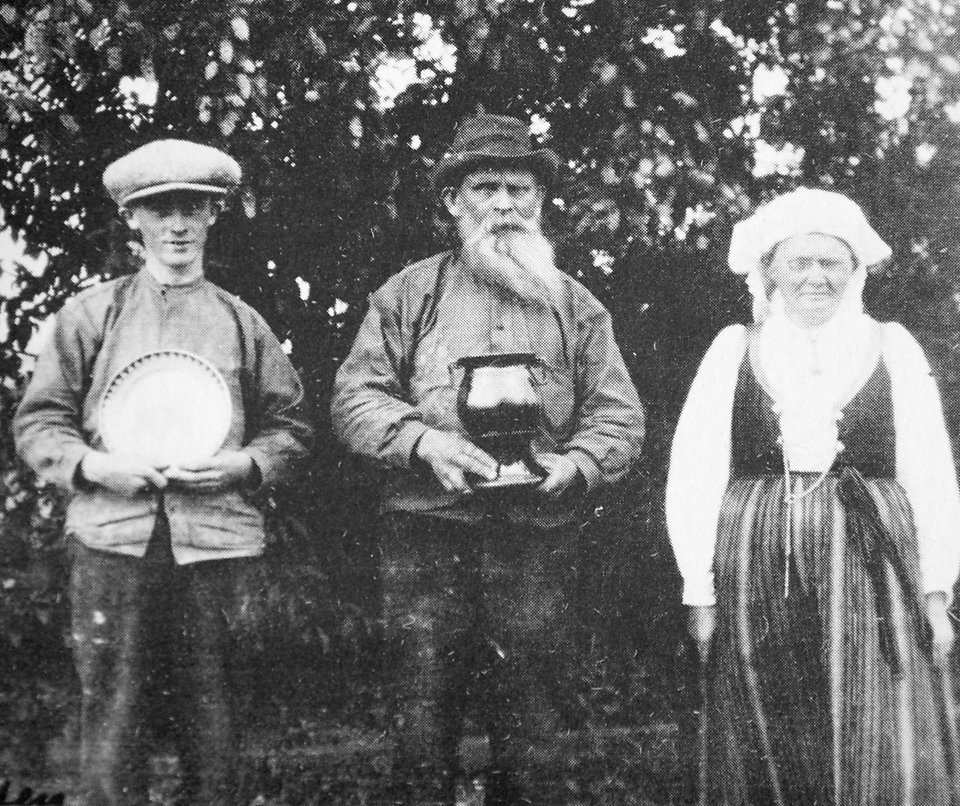 Svartvitt foto. Albert, Axel och Elna Elfstrand står framför ett träd. Albert och Axel håller i ett fat och en kruka.