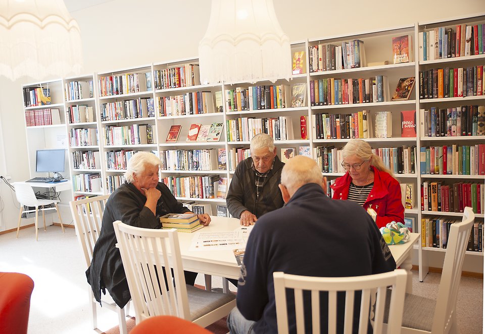Interiör från Lövestads bibliotek. 4 personer sitter runt ett bord och samtalar. I bakgrunden bokhyllor.